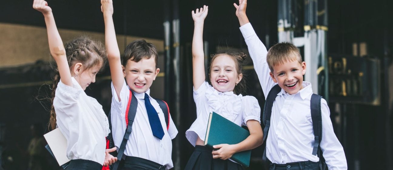 School children with their hands up looking happy