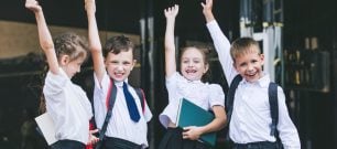 School children with their hands up looking happy